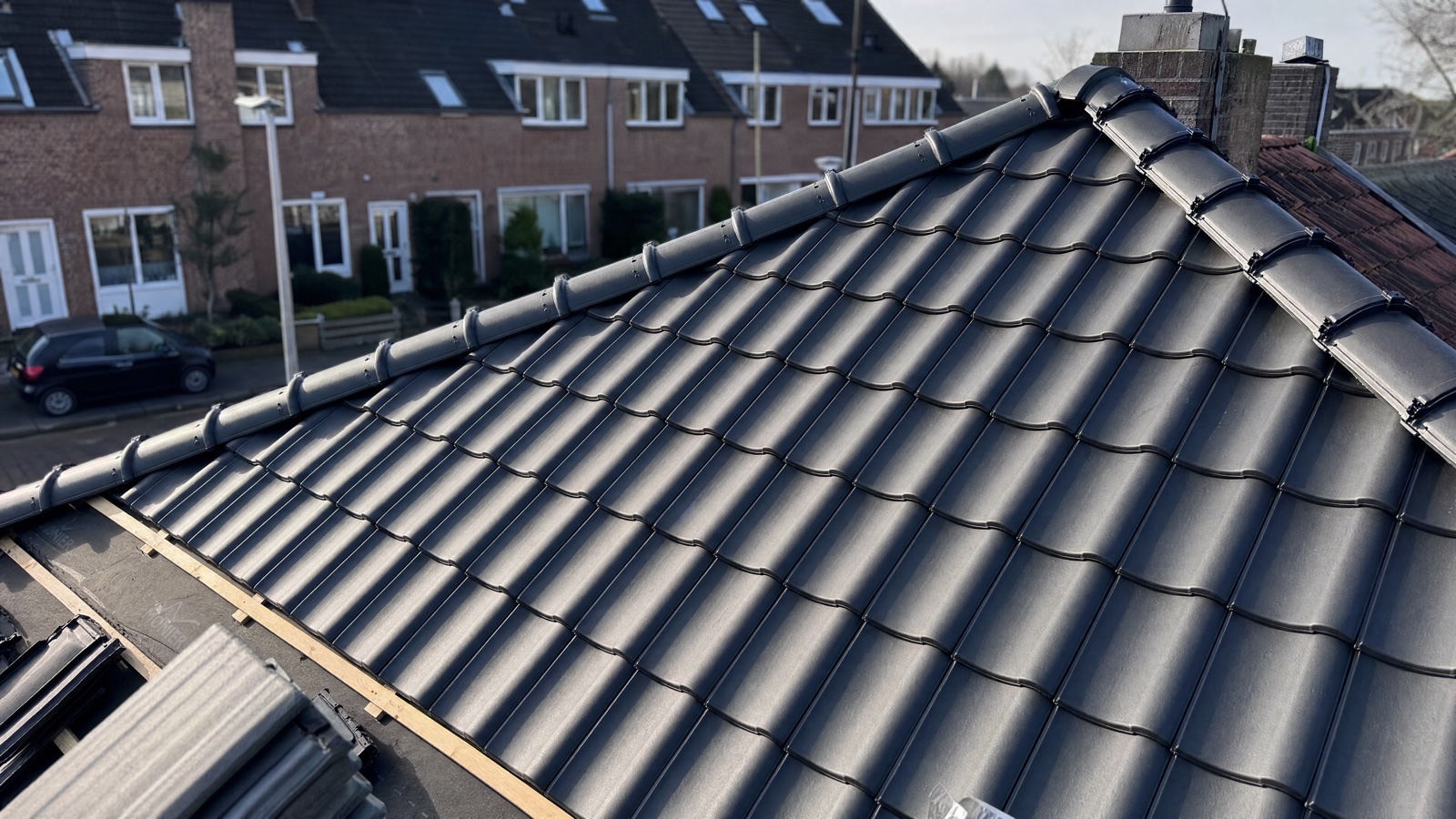 Nieuw, antracietkleurig pannendak in aanleg, met uitzicht op een straat met Nederlandse rijtjeswoningen